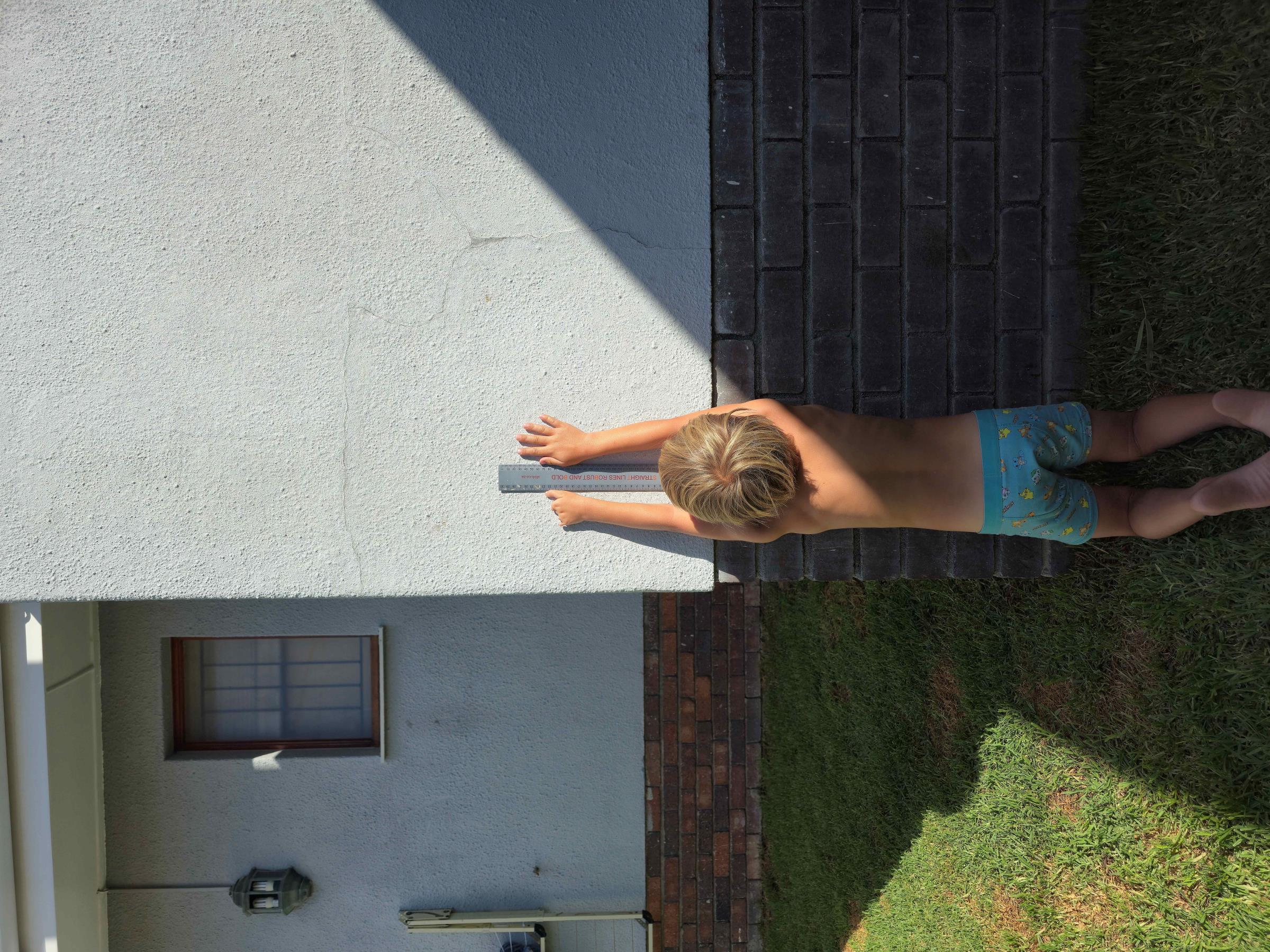 Noah reaching up against a white wall, showing his left hand from behind and the ruler for scale